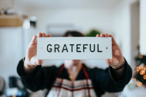 Woman holding a small sign that says "GRATEFUL". This photo is on www.becomingstoic.net in a post called "Always Be Grateful".