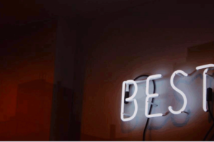 Dark wall with a neon sign glowing white that says "BEST". This is used in a post on how Stoicism helps you on being your best. It is on www.becomingstoic.net in a post called "How To Be you Best".