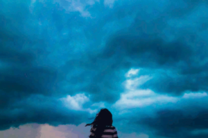 back view of a woman in a sweater and long dark hair facing a dark stormy looking sky. This photo is used on www.becomingstoic.net in a post called "being Fearless".