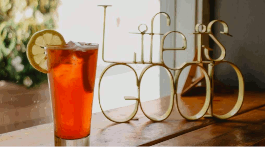 A cool looking glass of tea with a lemon slice on the rim to the left of the table. On the right side of the table is a brass looking statue that is shaped in the words "Life is Good". Focusing on a good life is an important Stoic concept. This photo is on www.becomingstoic.net on a post called "Focusing On A Good Life".