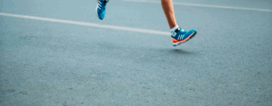 The legs of a runner in blue running shoes as they stride down a paved road. This photo is used on www,becomingstoic.net in an article called "Marathon or Sprint".