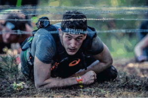 Man crawling through dirt under barbwire in Spartan Race. This photo is used on www.becomingstoic.net in an article named "Building Mental Toughness".